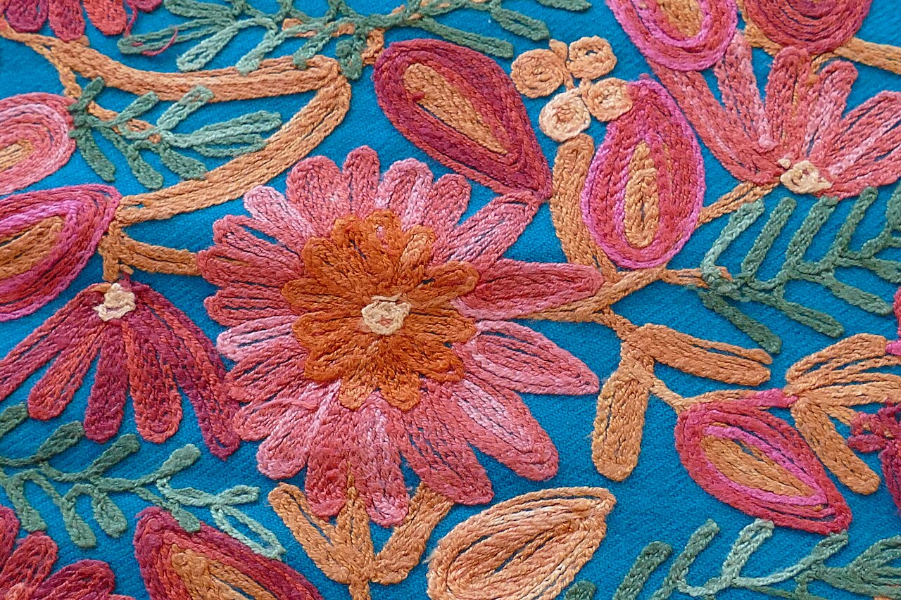 Real close-up photograph of colourful floral chain-stitch embroidery on a turquoise wool shawl from Kashmir